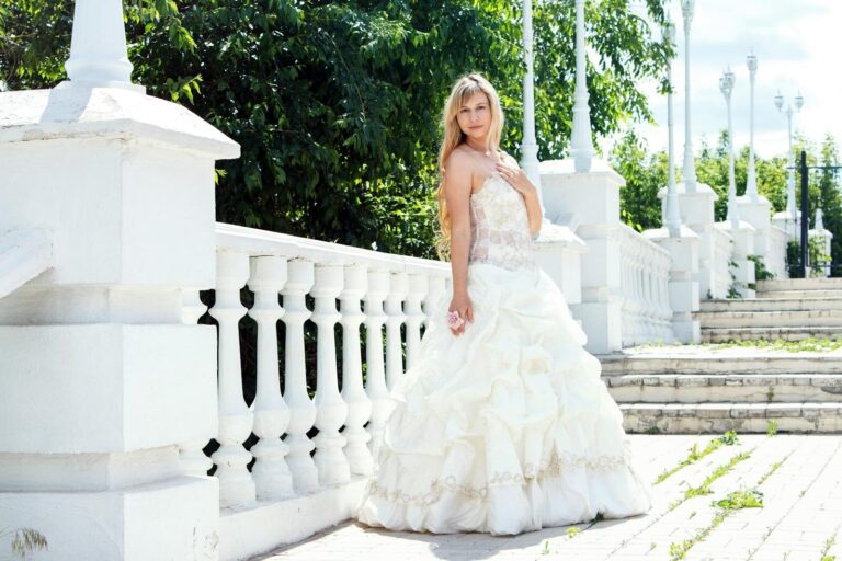 A beautiful bride in a luxurious white wedding gown posing gracefully outdoors.
