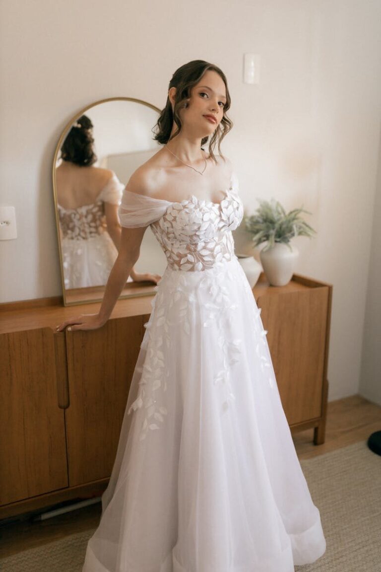 A beautiful bride in a stylish white gown poses indoors, showcasing bridal elegance and charm.