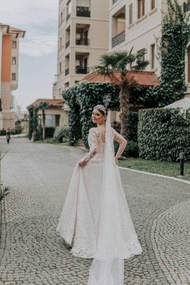 A beautiful bride in a long white gown and veil stands smiling on a cobblestone street in Azerbaijan.