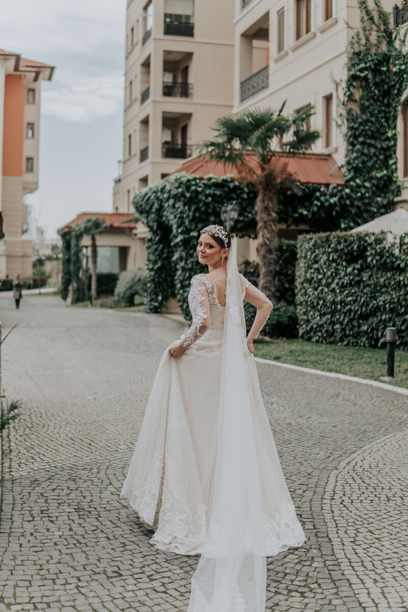 A beautiful bride in a long white gown and veil stands smiling on a cobblestone street in Azerbaijan.