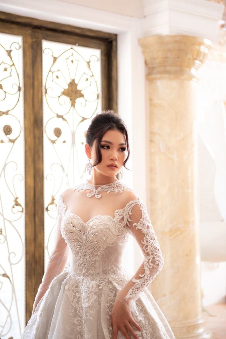 A beautiful bride in an elegant lace gown posing indoors by ornate doors.