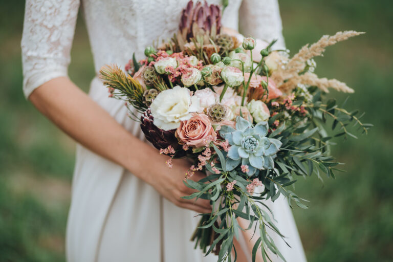 bride in a dress standing in a green garden and holding a wedding bouquet of flowers and greenery
